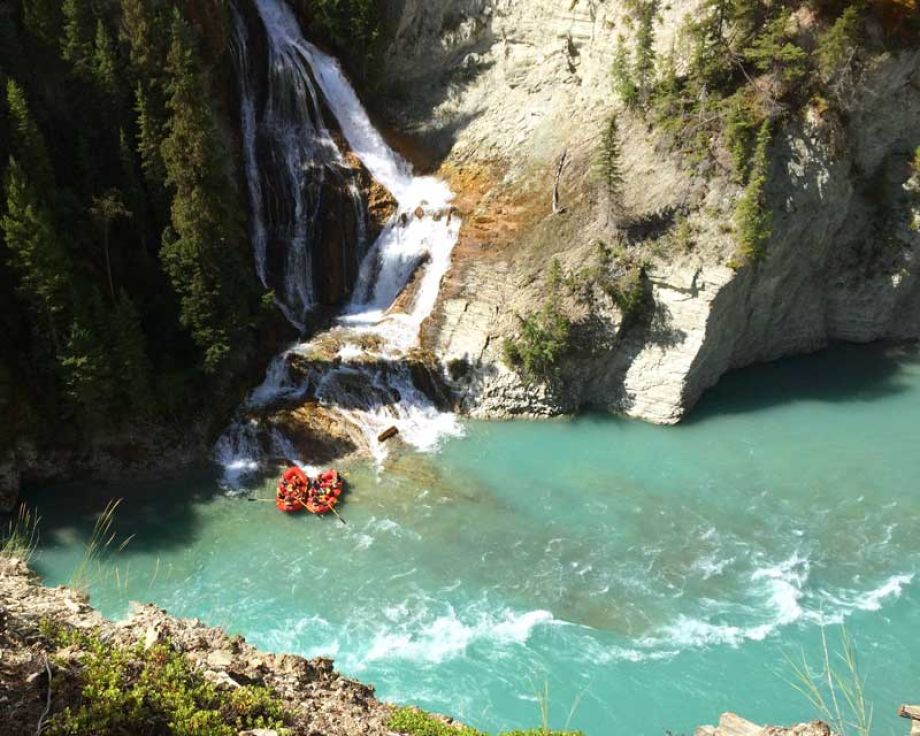 Two red rafts in the river next to a waterfall.