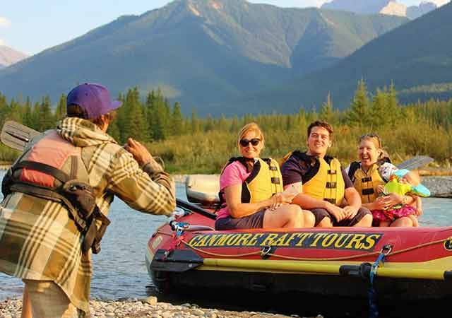 A guide taking pictures of guests in a raft with mountains in the background.