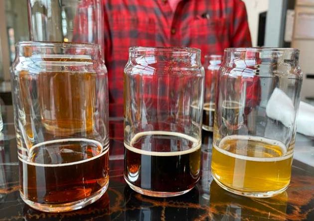 Medium, dark and light beer in clear glasses with a person in a red shirt behind.